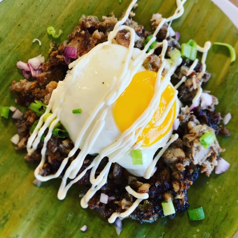 Filipino sisig with a fried egg and mayonnaise drizzle, served on a banana leaf.