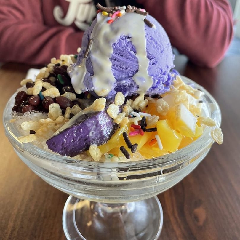 Halo-halo dessert with ube ice cream, red beans, fruit, and sprinkles in a glass bowl.