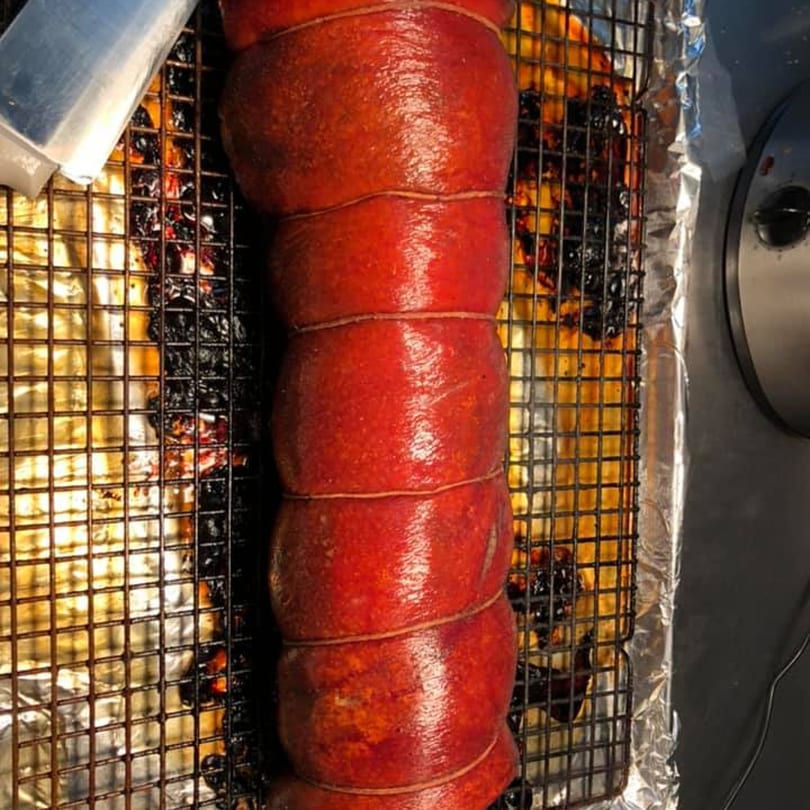 A large, red, tied meat roast cooking on a metal rack over a foil-lined pan.