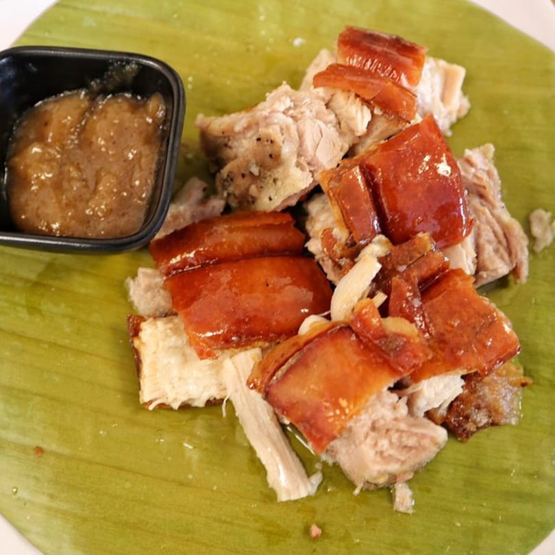 Crispy Filipino lechon (roast pork) with dipping sauce, served on a banana leaf.