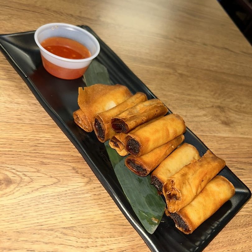 Crispy Filipino lumpia rolls with a sweet chili dipping sauce on a black rectangular plate.