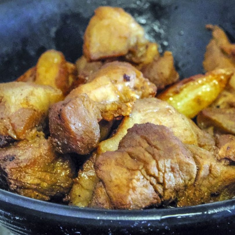Close-up of golden-brown fried pork belly and potatoes in a dark pan, a Filipino dish.